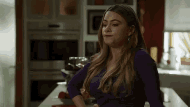 a woman in a purple top is standing in a kitchen .