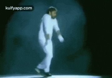 a man in white pants and gloves is dancing on a stage in a dark room .