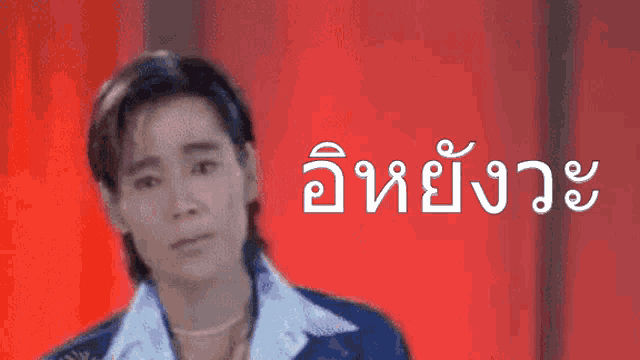 a man in a blue jacket stands in front of a red background with a foreign language written on it