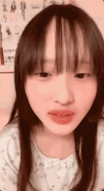 a young girl with long hair and bangs is making a funny face while looking at the camera .