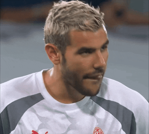 a man with a beard is wearing a white shirt with a red puma logo on the front