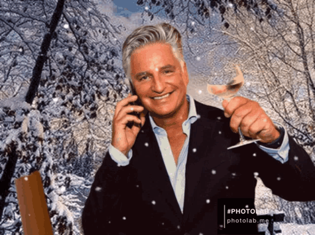 a man in a suit is talking on a cell phone and holding a glass of wine