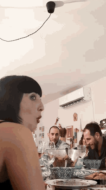 a woman with a surprised look on her face sits at a table with two men