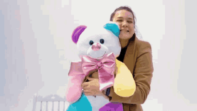 a woman is holding a colorful teddy bear with a bow on it
