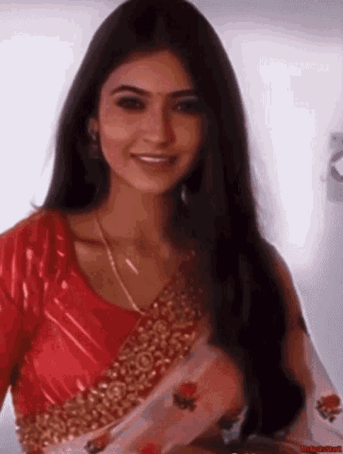 a woman wearing a red top and a white saree is smiling .