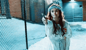 a woman in a white dress is holding a gun and pointing it at the camera .