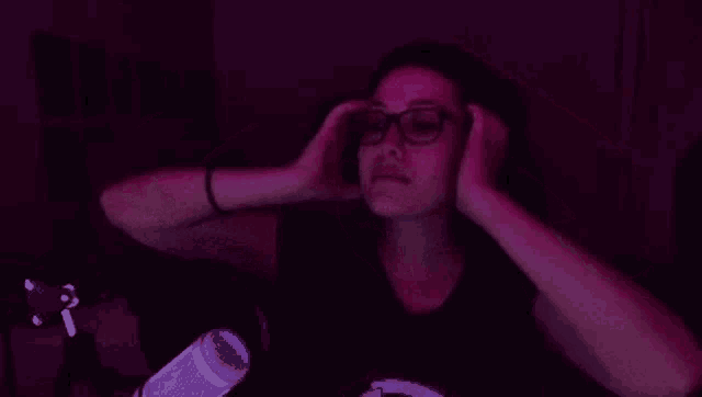 a woman wearing glasses is sitting in front of a microphone and holding her hair .