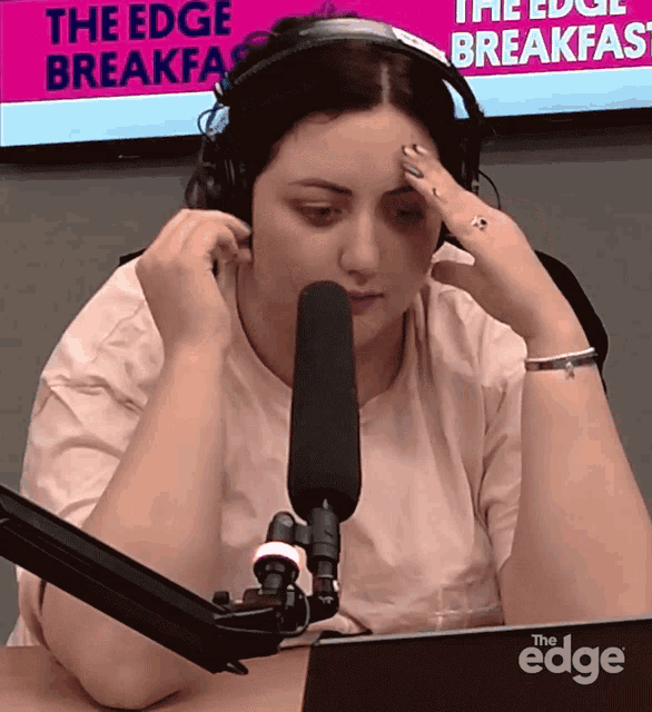 a woman wearing headphones sits in front of a microphone in front of a sign that says " the edge breakfast "