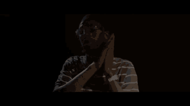 a man wearing glasses and a striped shirt is making a face in the dark