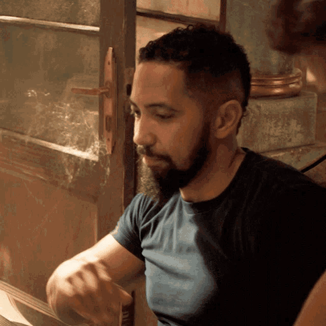 a man with a beard is sitting in front of a glass door