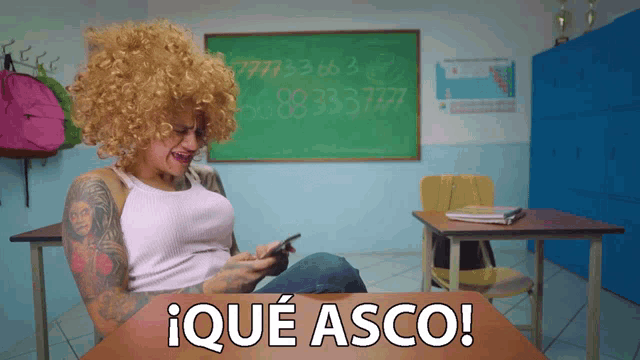 a woman in a wig sits at a desk in front of a chalkboard that says ' iqué asco '