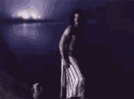 a shirtless man in a striped skirt is standing in front of a body of water