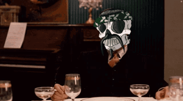 a man with a skull on his head sits at a table