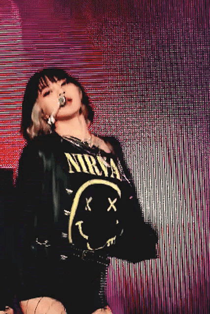 a woman singing into a microphone wearing a black nirvana shirt