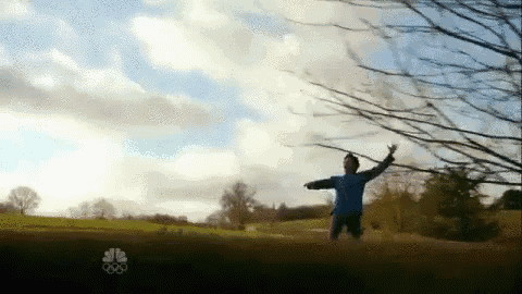 a man in a blue shirt is jumping in the air in a field with a nbc logo in the background