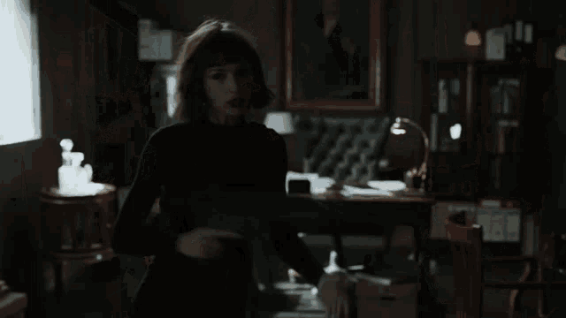 a woman in a black dress is holding a gun in her hand in a dark room .