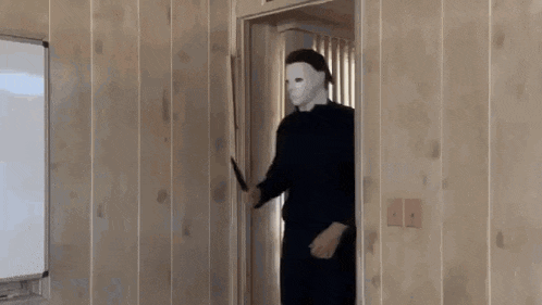 a man in a mask is holding a knife in a room .