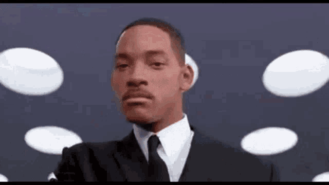 a man in a suit and tie is standing in front of a bunch of white circles .