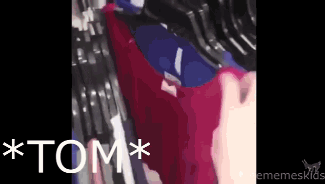 a person is holding a red shirt in front of a row of blue shirts and the word tom is on the bottom right