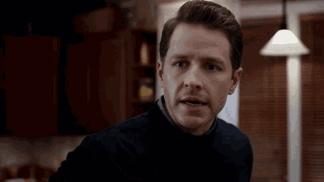 a man in a black sweater is standing in a kitchen looking at the camera