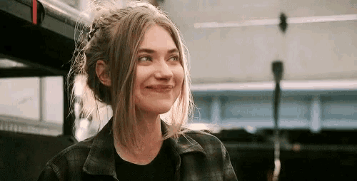 a woman is smiling while sitting on a bus and wearing a plaid shirt .