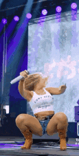a woman in a white tank top and denim shorts is kneeling down on a stage holding a microphone .