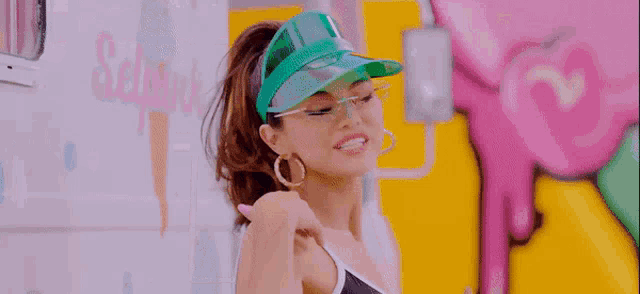 a woman wearing a green hat , sunglasses and hoop earrings is blowing a kiss .