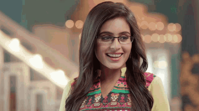 a woman wearing glasses and a colorful top smiles for the camera