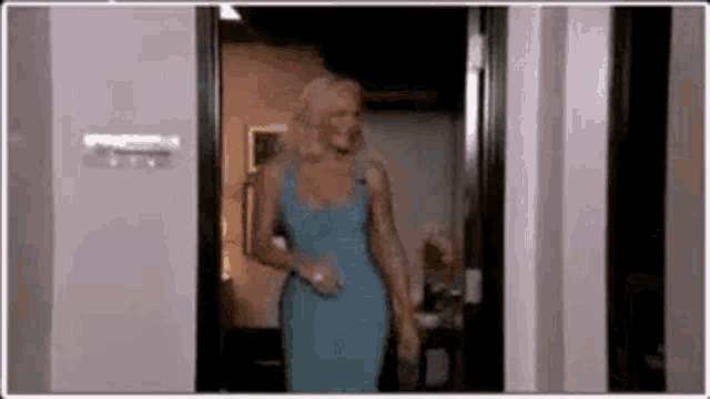 a woman in a blue dress is standing in a doorway holding a glass .