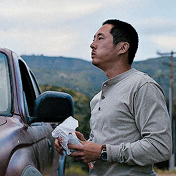 a man in a gray shirt is standing next to a car