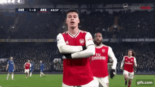 a soccer player wearing a fly emirates jersey stands on the field with his arms crossed