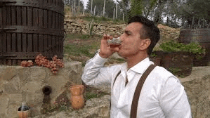 a man is drinking a glass of wine in front of a wooden barrel .