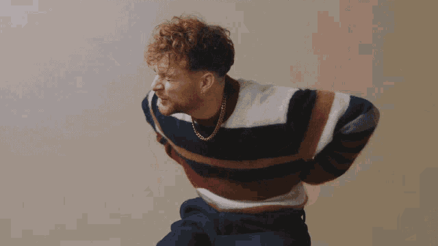 a man with curly hair is wearing a striped sweater and a chain around his neck