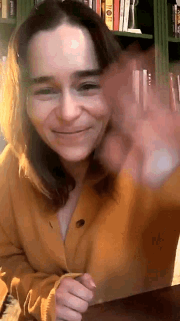 a woman wearing a yellow cardigan is smiling and waving