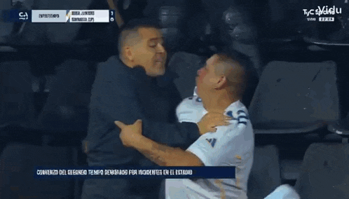 two men are hugging each other in front of a banner that says tfc aguila