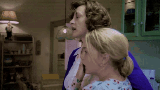 two women are standing next to each other in a kitchen with a lamp in the background