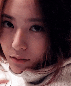 a close up of a woman 's face with a turtleneck sweater on looking at the camera .