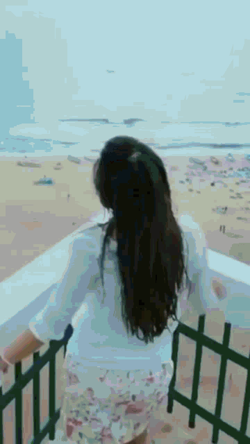 a woman stands on a balcony overlooking the beach