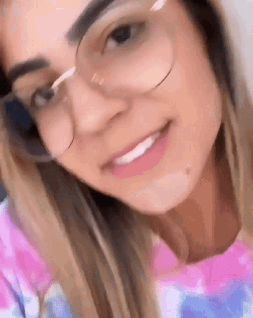 a woman wearing glasses and a tie dye shirt is smiling .