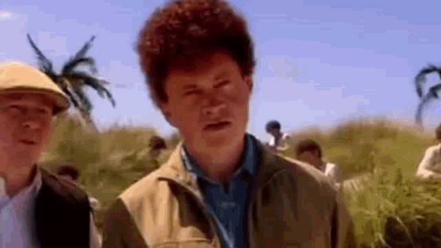 a man with red hair is standing in a field next to another man .