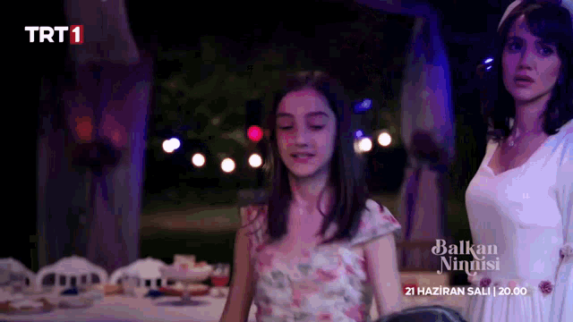 a woman in a white dress stands next to a young girl in a floral dress with trt1 on the bottom right