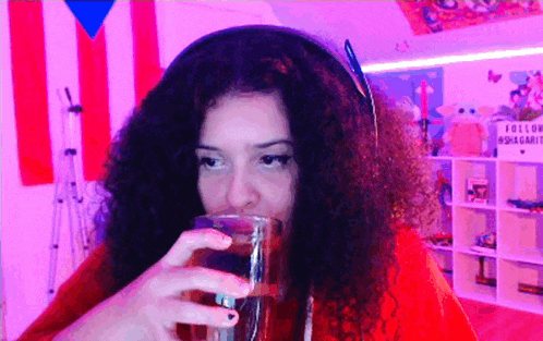 a woman wearing headphones drinks from a glass in front of a sign that says follow