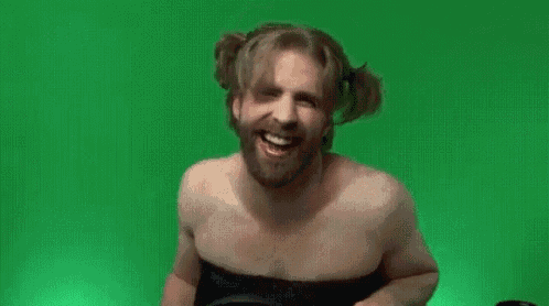 a shirtless man with a beard is wearing a black dress and smiling .