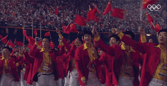 a group of people wearing red jackets and yellow shirts are waving red flags in front of an olympic logo