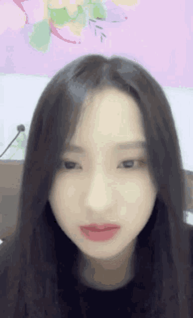 a woman with long black hair is looking at the camera with a pink background behind her .