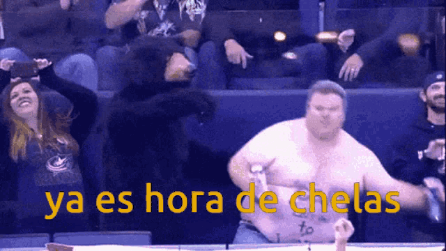 a man without a shirt is dancing in front of a crowd and the words ya es hora de chelas are above him