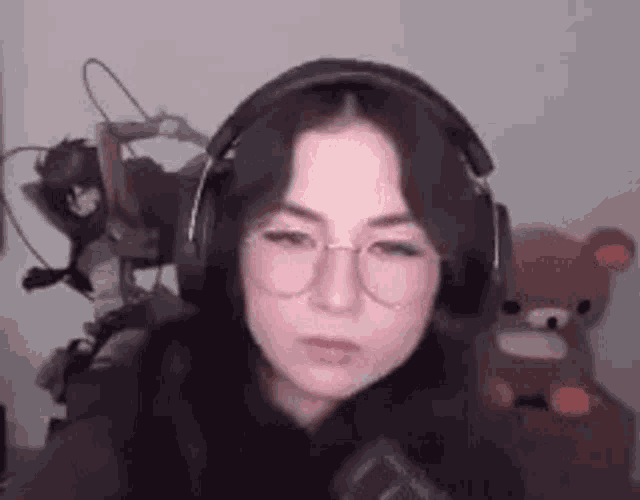 a woman wearing headphones and glasses is sitting in front of a stuffed animal .