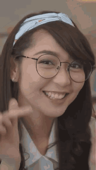 a woman wearing glasses and a headband is smiling and waving