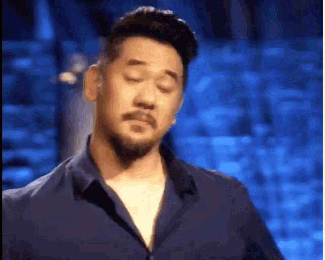 a man with a beard and a blue shirt is making a funny face .