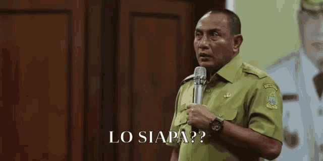 a man in a green shirt is holding a microphone and saying lo siapa ??